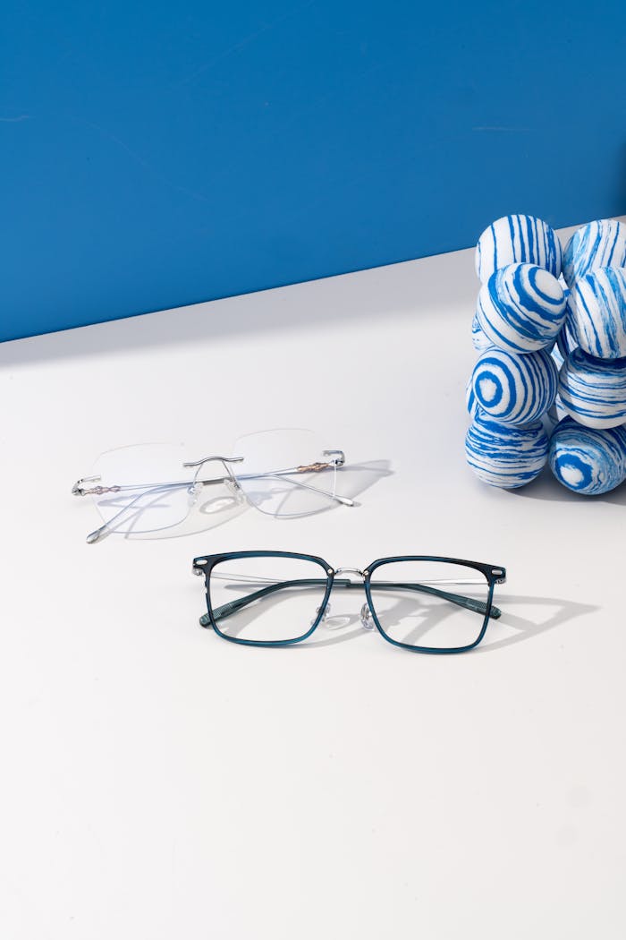 Modern eyeglasses displayed on white surface with artistic blue ball sculpture. Ideal for fashion and lifestyle themes.